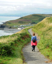 A woman strolling along a coastal path heading towards a seaside village.
