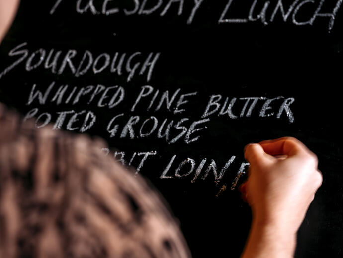 Close up of human hand writing menu on blackboard