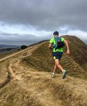 Trail runner running along a trail at the top of a steep hill