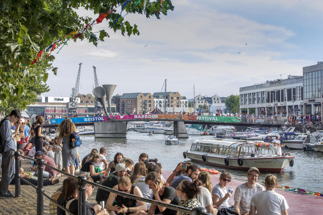 Crowds of people sitting on the harbourside in Bristol, watching ships go past