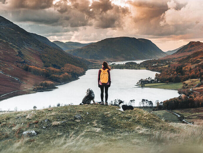 Woman standing with two dogs looking down at a lake in a valley