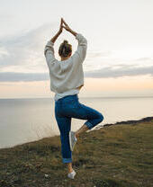 Donna in posizione yoga in piedi sulla cima di una scogliera a picco sul mare