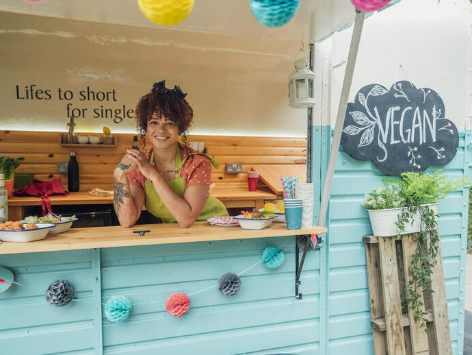 Young woman stood in the hatch of a food truck smiling, ready to serve