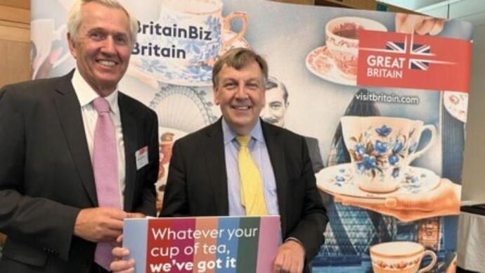 Nick De Bois posing in front of VisitBritain promotional materials