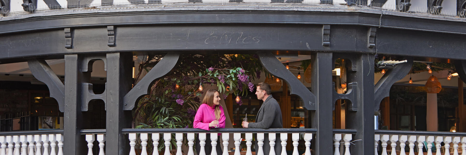 A man and a woman have a drink and talk on the balcony at a local cafe.