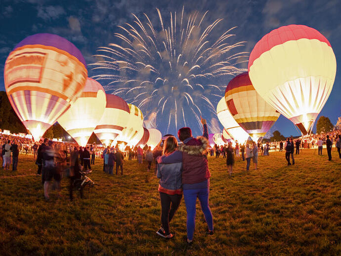 Couple watching grounded hot air balloons and fireworks in the night sky