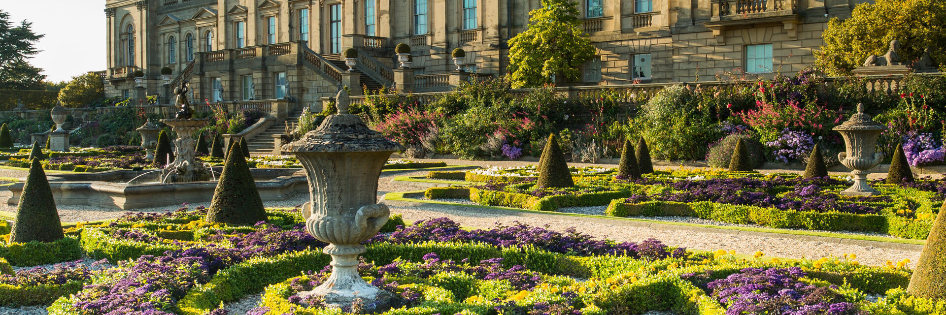 A formal garden with statues and low hedges in front of a stately house