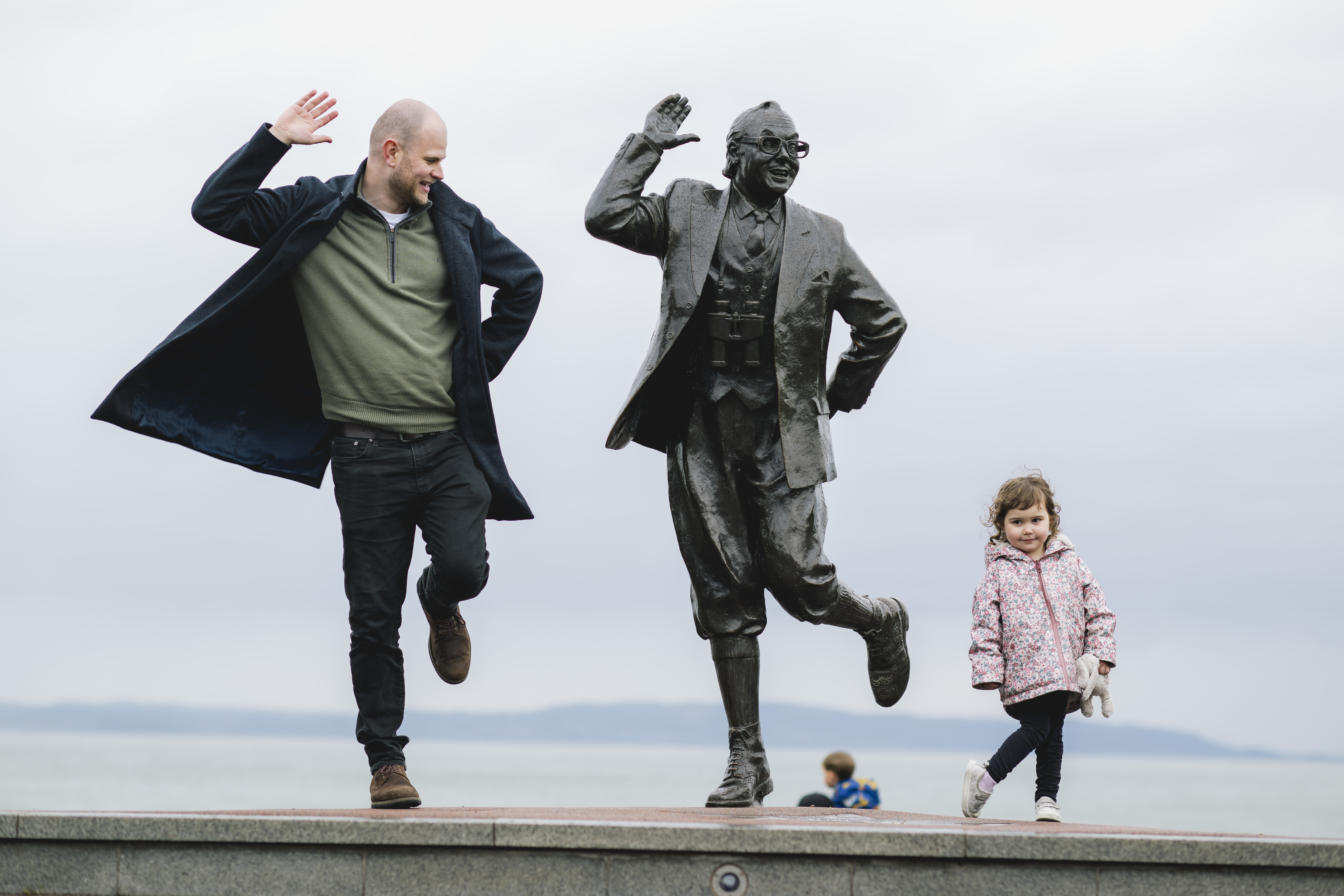 View of man, female child and statue of a man in front of the sea