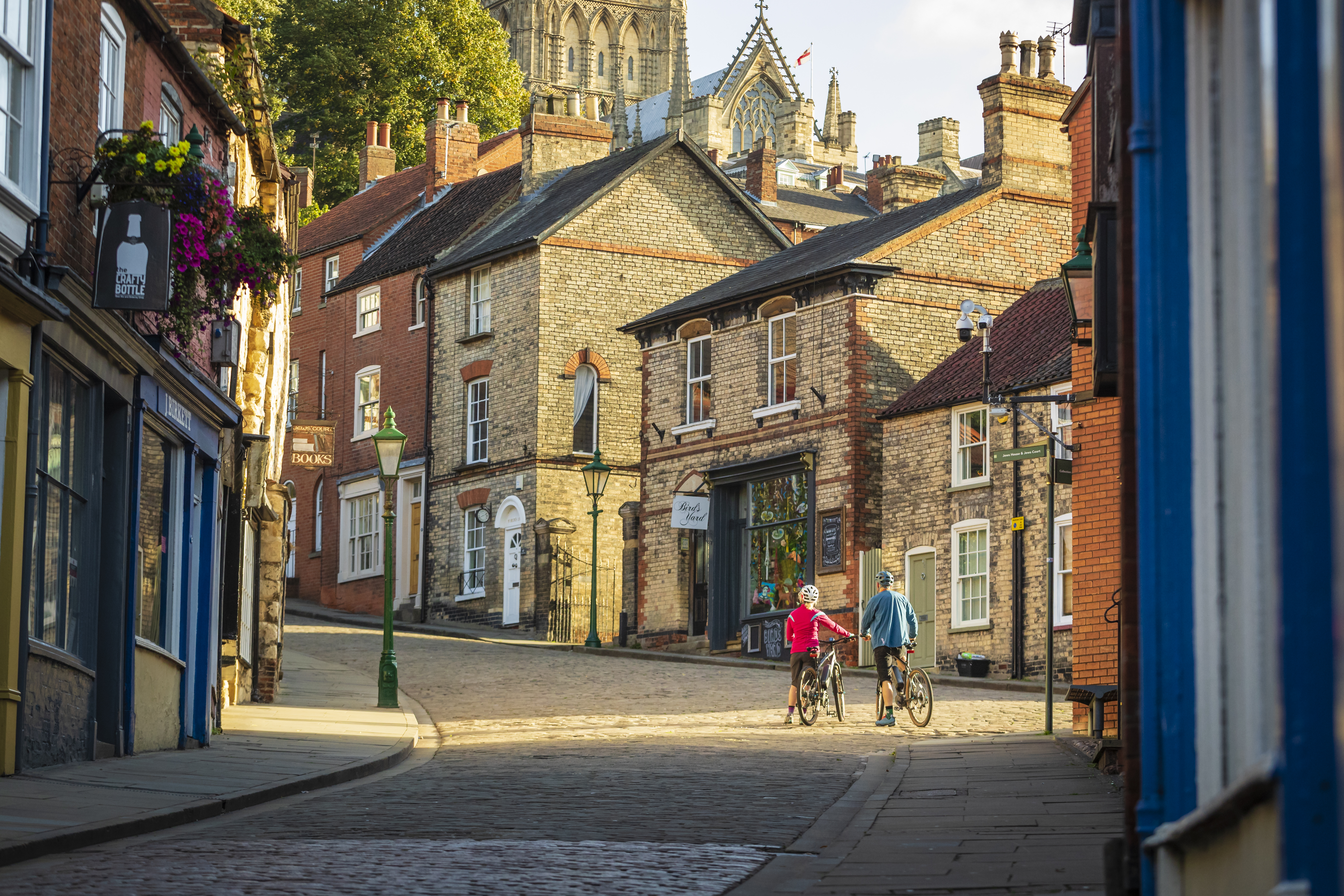 Zwei Radfahrer, die mit ihren Fahrrädern in Lincoln bergauf gehen, im Hintergrund Lincoln Castle