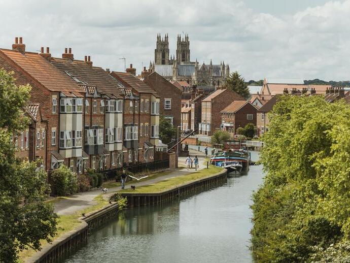 A canal with moored boats winding through a pretty English town.