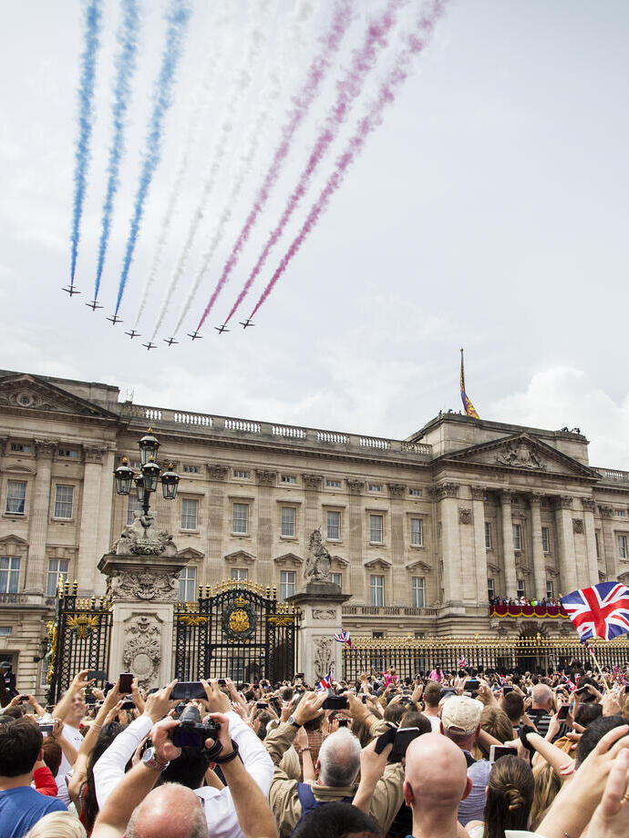 Jets mit farbigen Rauchfahnen fliegen in Formation über Menschenmengen und einen Palast