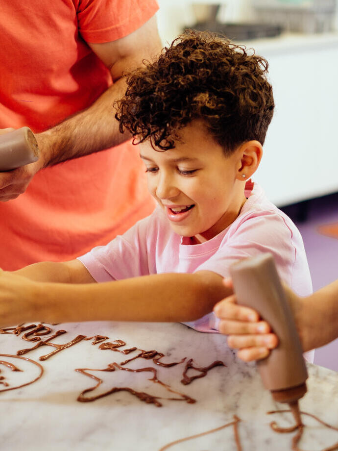 A boy, with curly hair, squeezing chocolate out of a bottle