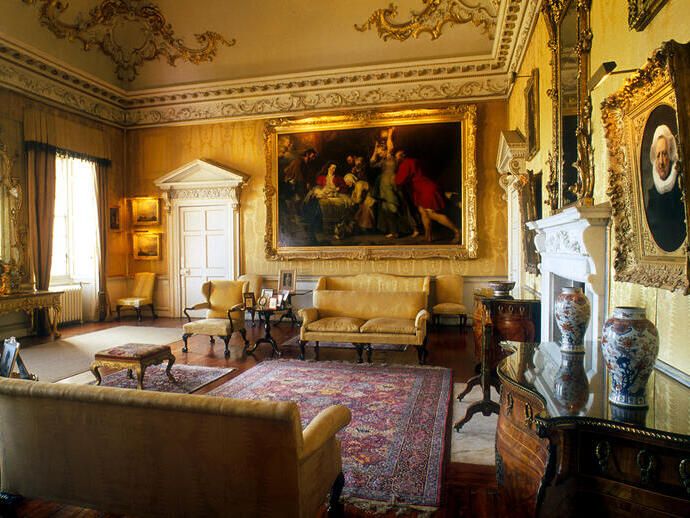 An ornate drawing room in a stately home with yellow walls, a red rug and other luxurious fittings.