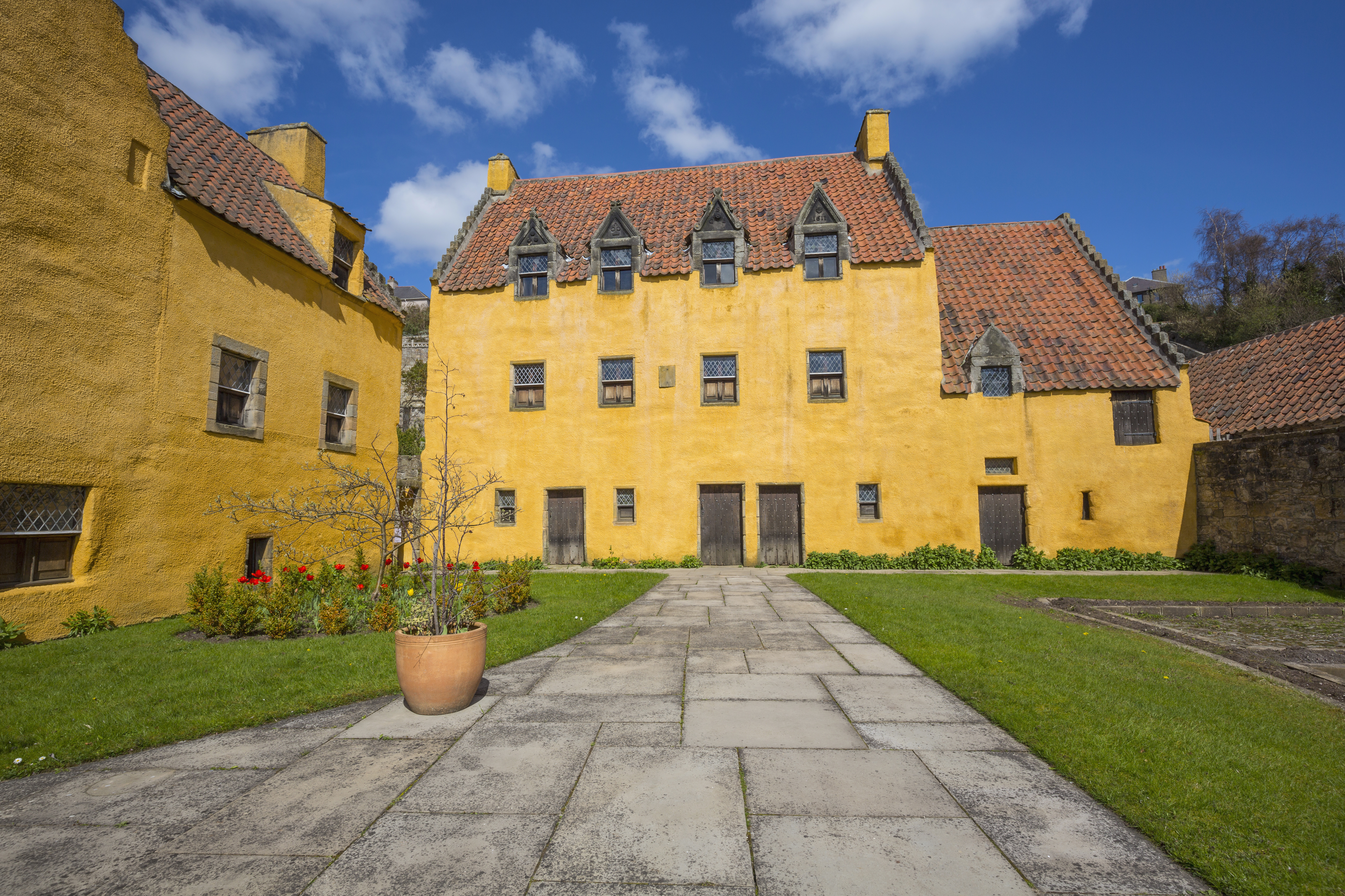 An small, rustic palace painted yellow with red roof tiles and a small lawn on a sunny day.
