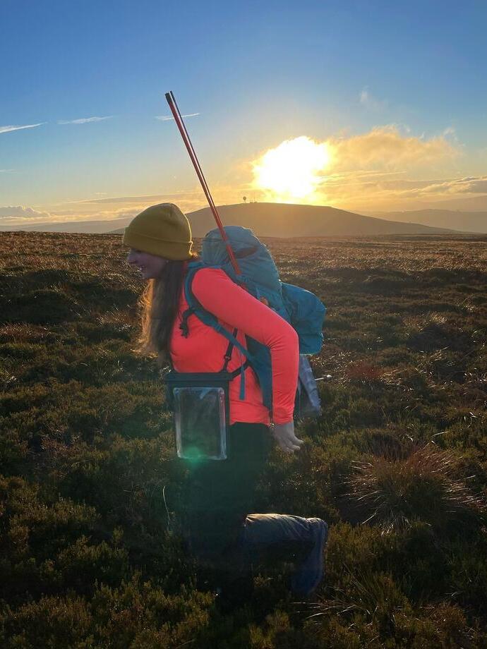 Female hiker with a backpack and walking poles, hiking through the countryside of Kilder in Northumberland at sunrise