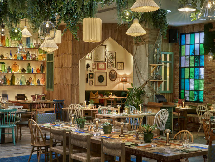 Tables set inside a restaurant with hanging lamps and green foliage.