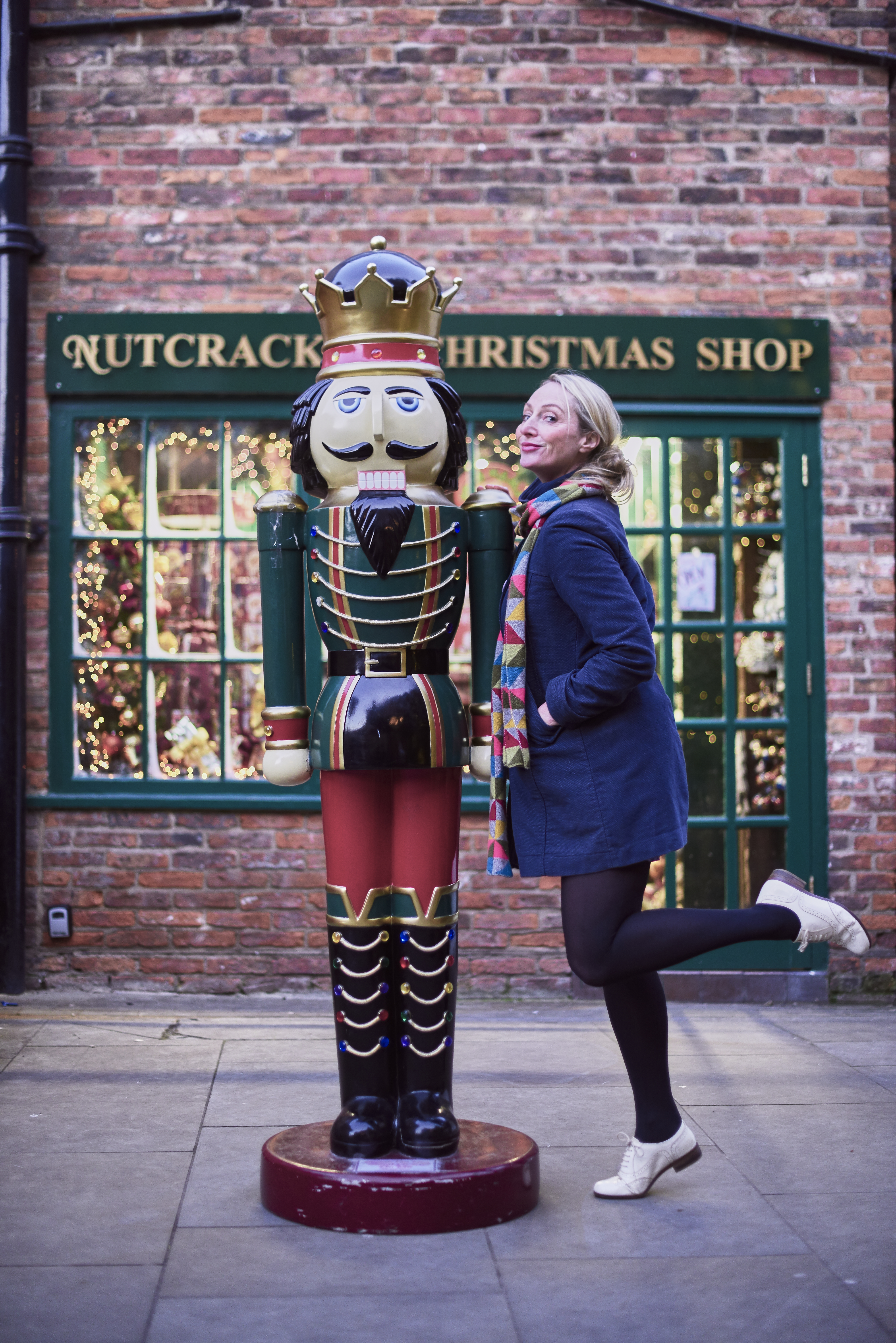 Woman posing beside a nutcracker prince statue, outside a christmas shop