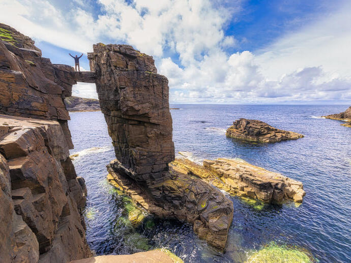 Man straddling two sea stacks overlooking a rocky outcrop and the ocean