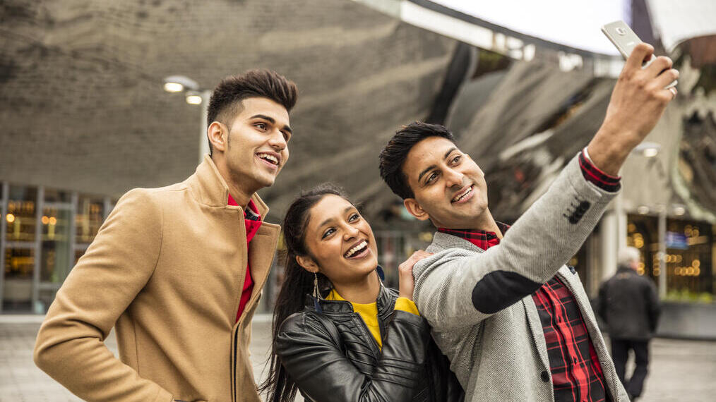 Three young people taking selfie outside building entrance