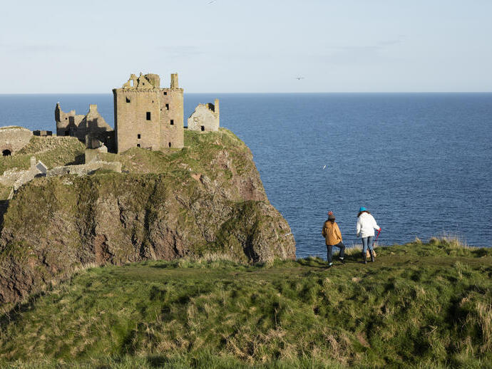Two women stood on a clifftop, near a castle and the sea