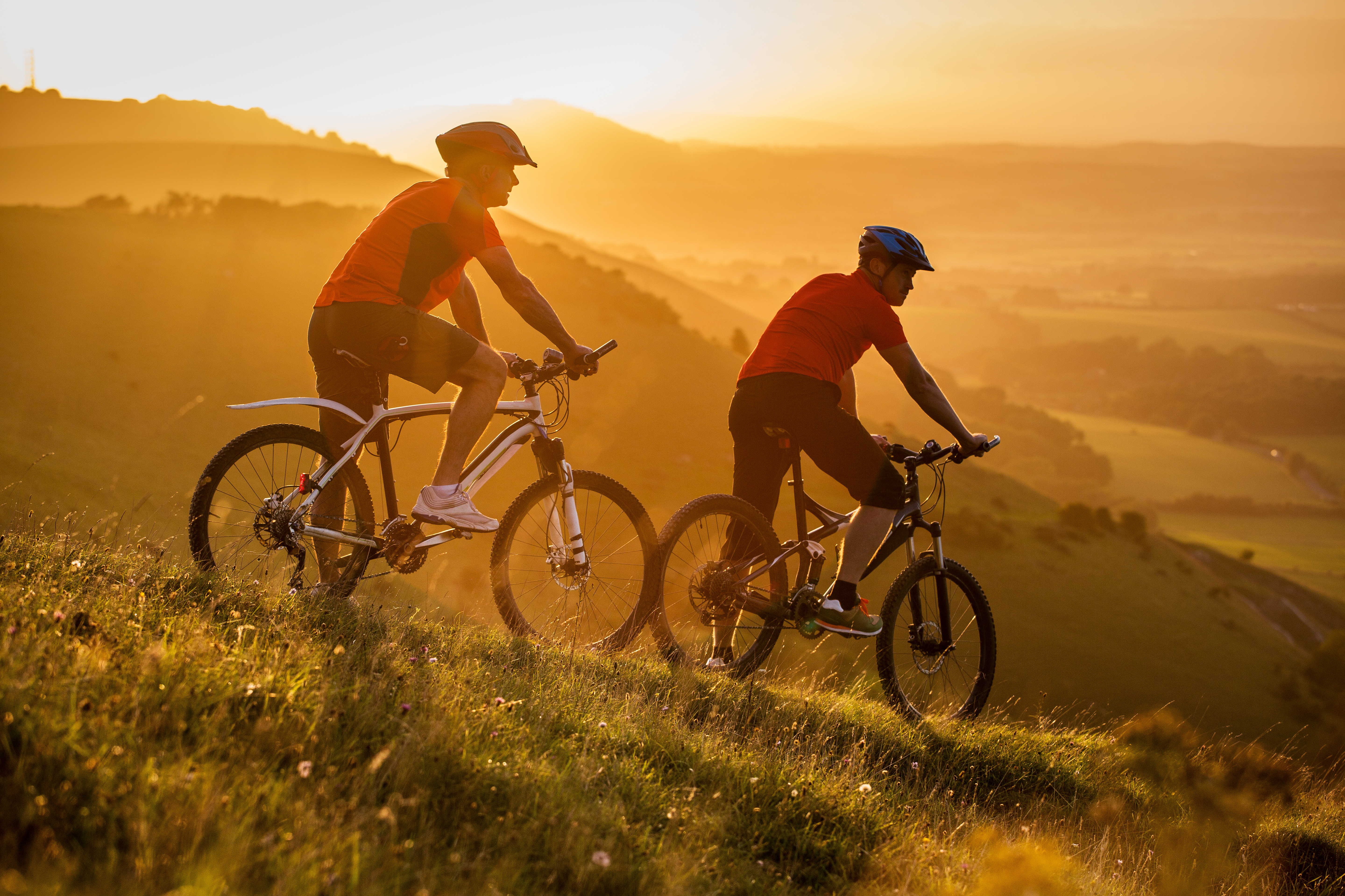 Two men on mountain bikes resting on the side of a hill at sunrise