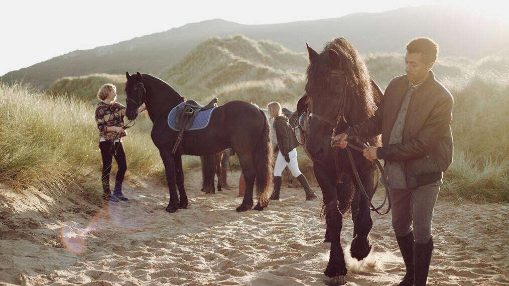 People leading horses along beach by their harness