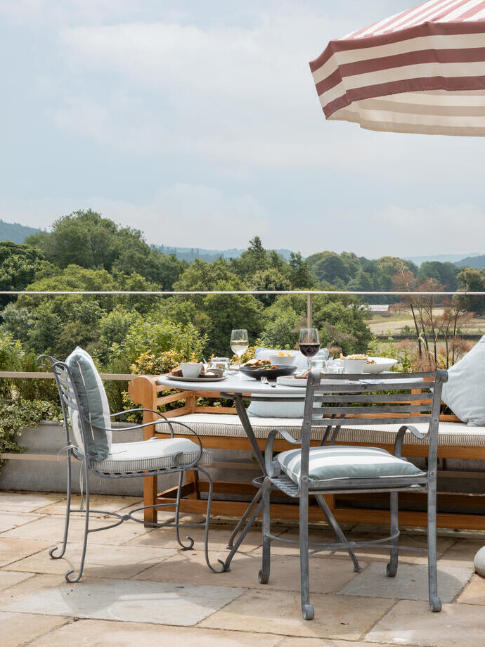 Tables on the patio with striped umbrellas overlooking the view at a luxury hotel on the grounds of a large country estate.