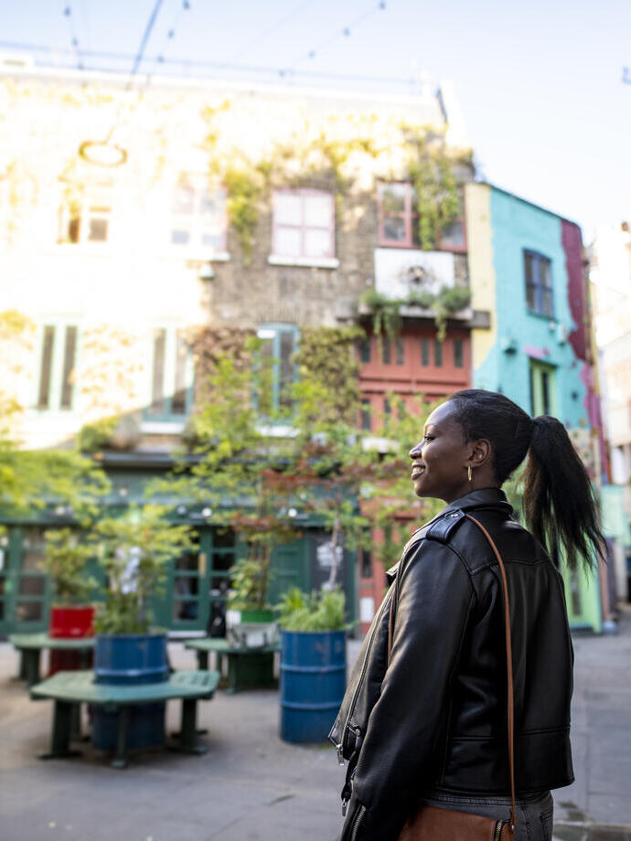 Female tourist exploring a London shopping courtyard with shops and outdoor seating.