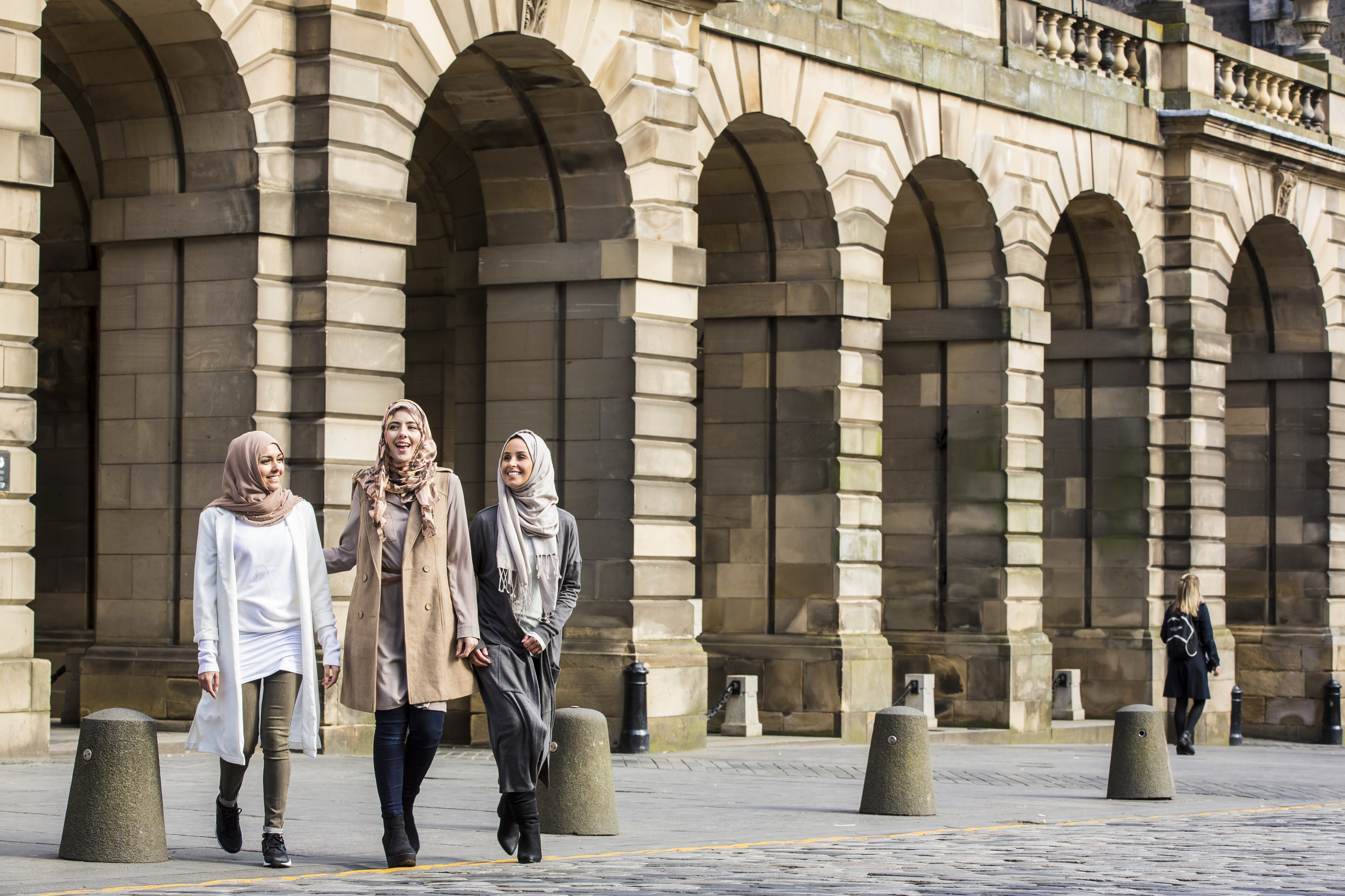 Three women walking by stone arches in a city