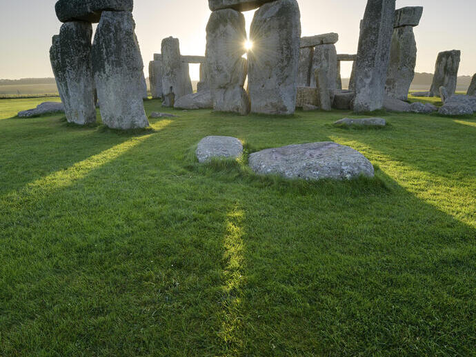 Large stone pillars arranged in circle on grass. Sunset