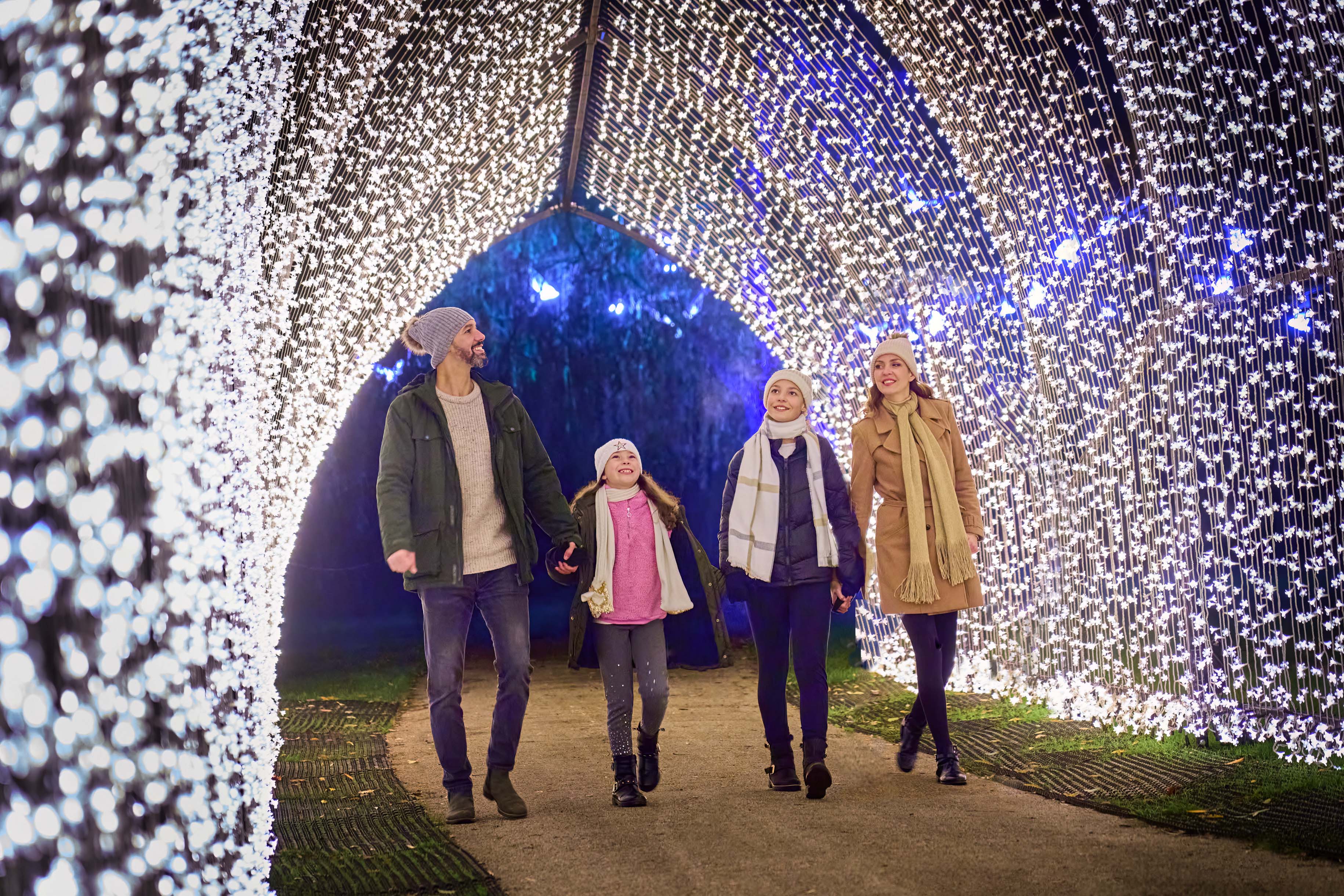 Family with children walk under a Christmas lights archway
