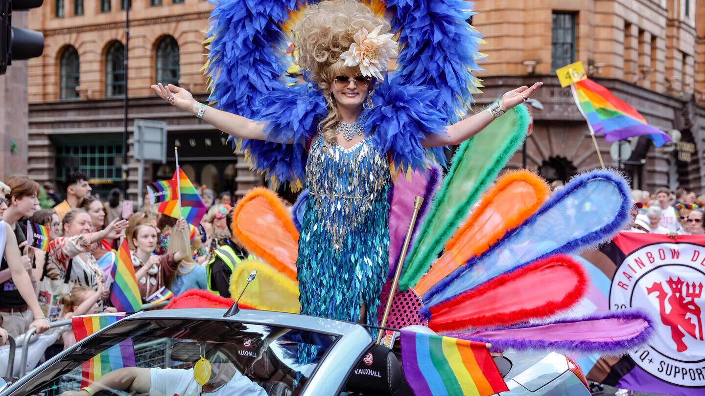 Persona in piedi in un'auto con abiti dai colori vivaci al Manchester Pride