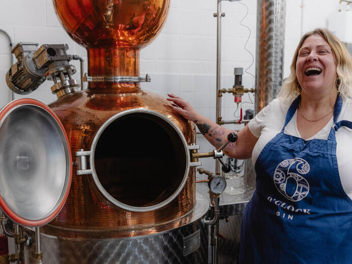 A female tour guide wears an apron and stands by a still at a distillery
