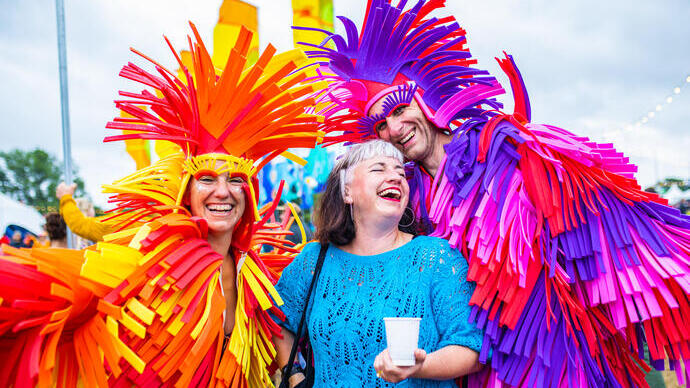 Drie mensen in kleurrijke kostuums die elkaar omhelzen en glimlachen tijdens een festival