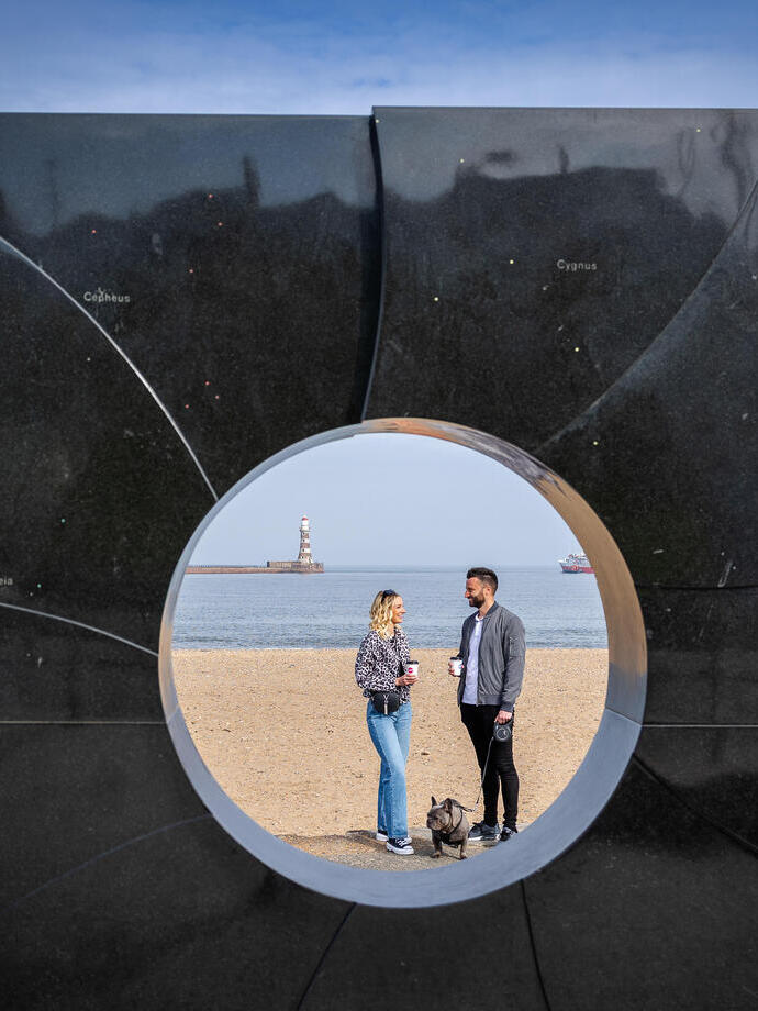 Two people seen through an art display on a beach sculpture trail.