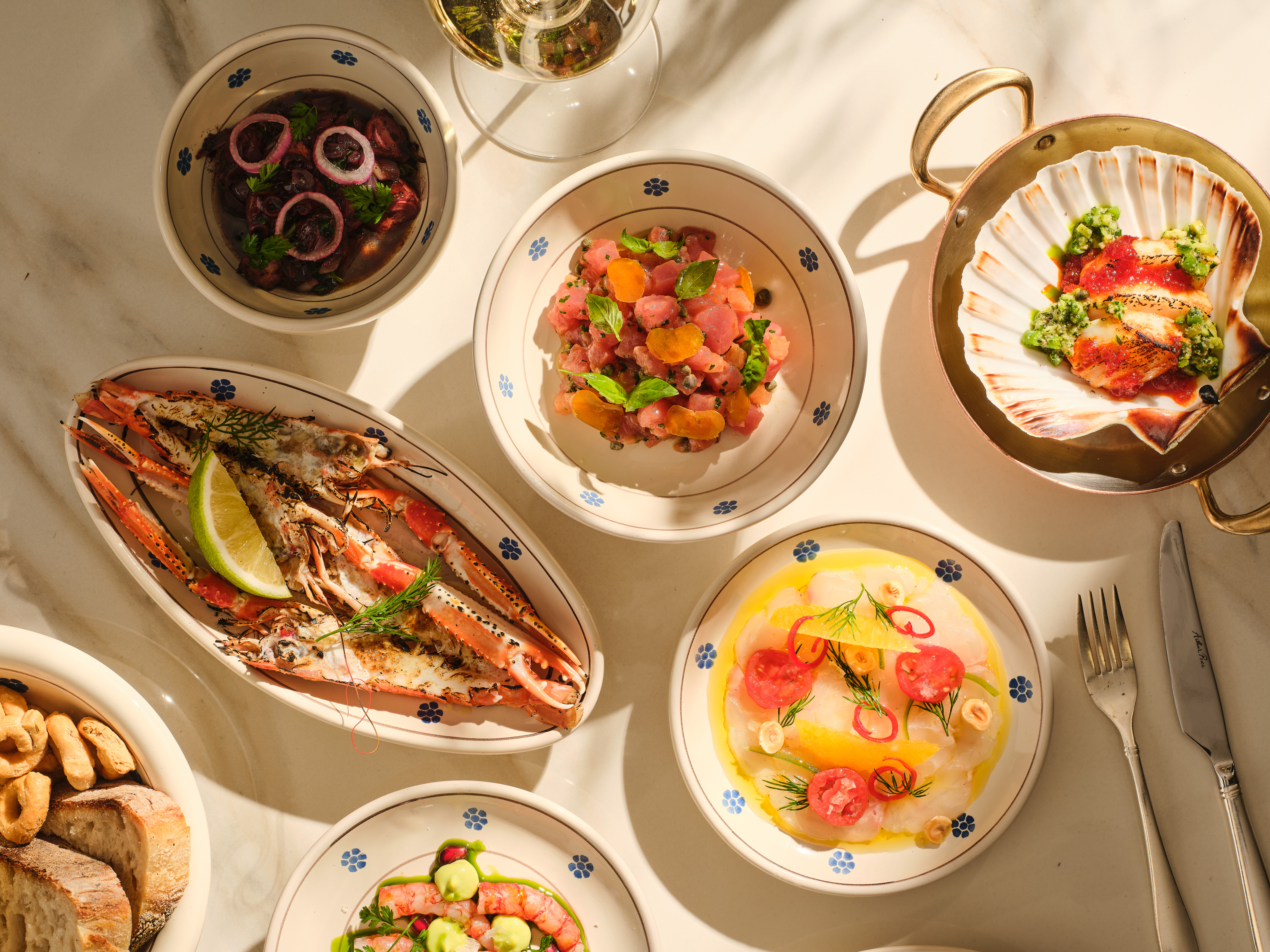 Un assortiment de plats méditerranéens et de fruits de mer sur une table en marbre, avec salades, fruits de mer et pain.