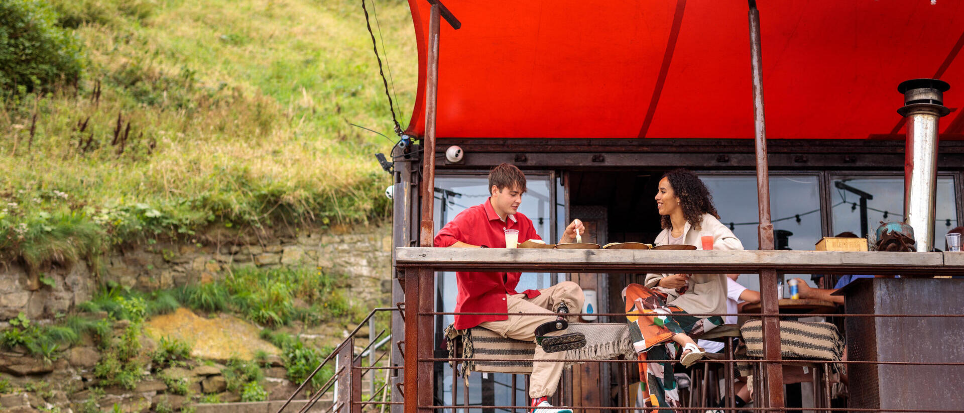 Friends enjoying food and drink at a beachside outdoor cafe.