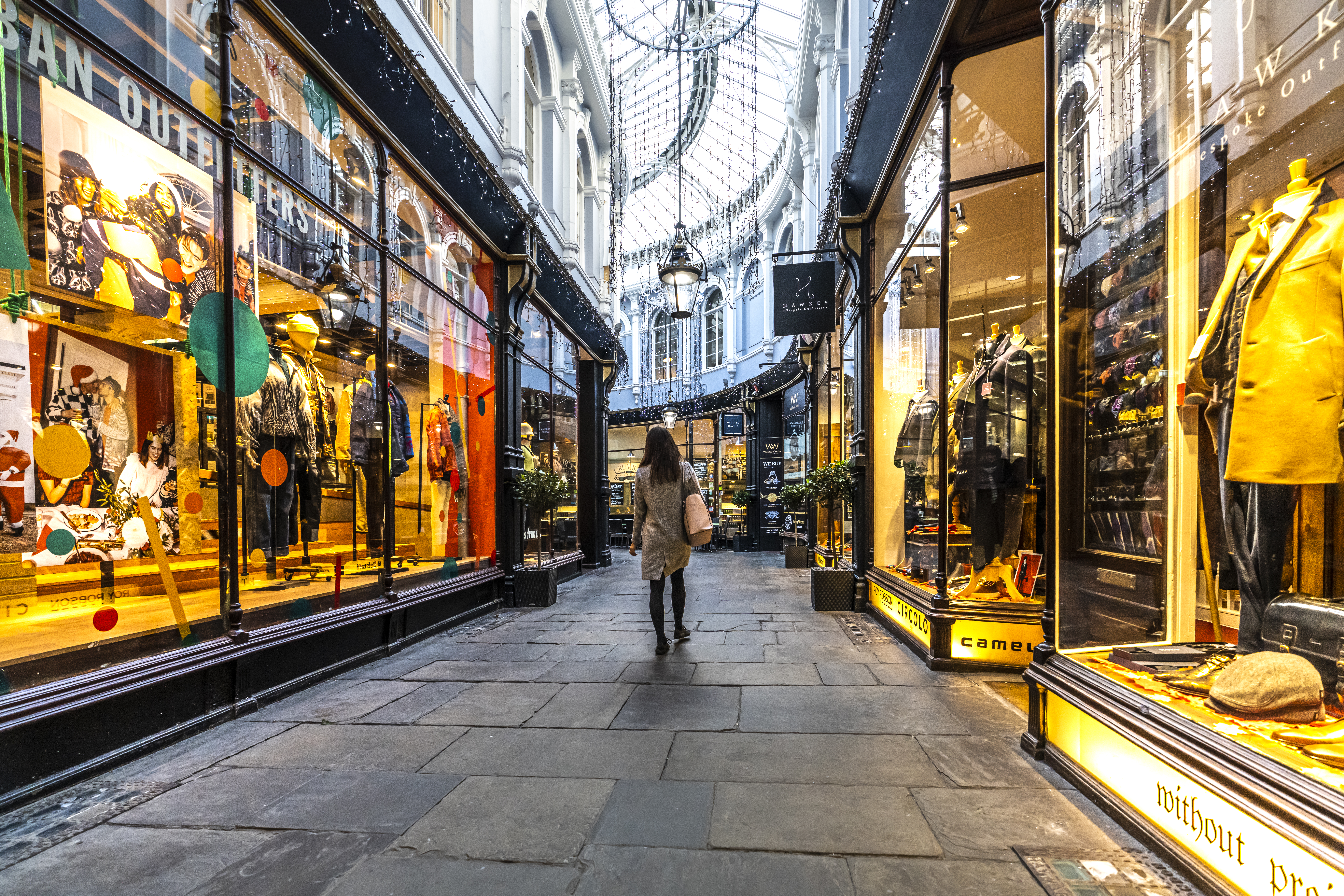 Woman walking through an arcade between shops, lit up from inside