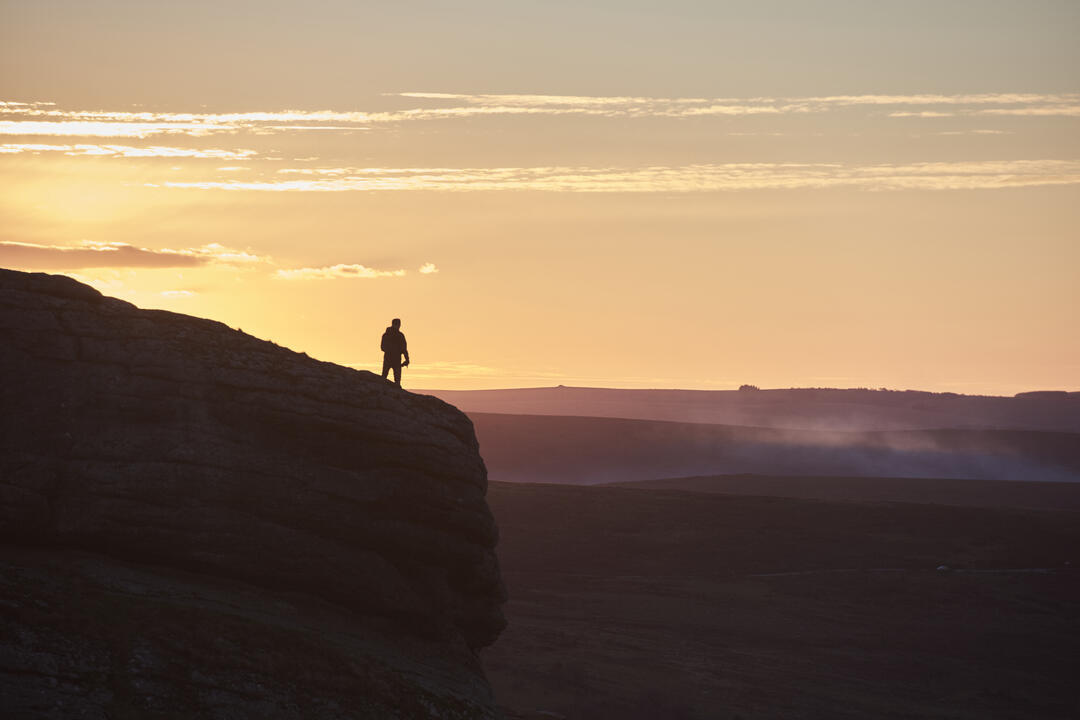 Silhouette of person hiking on large hill at sunset