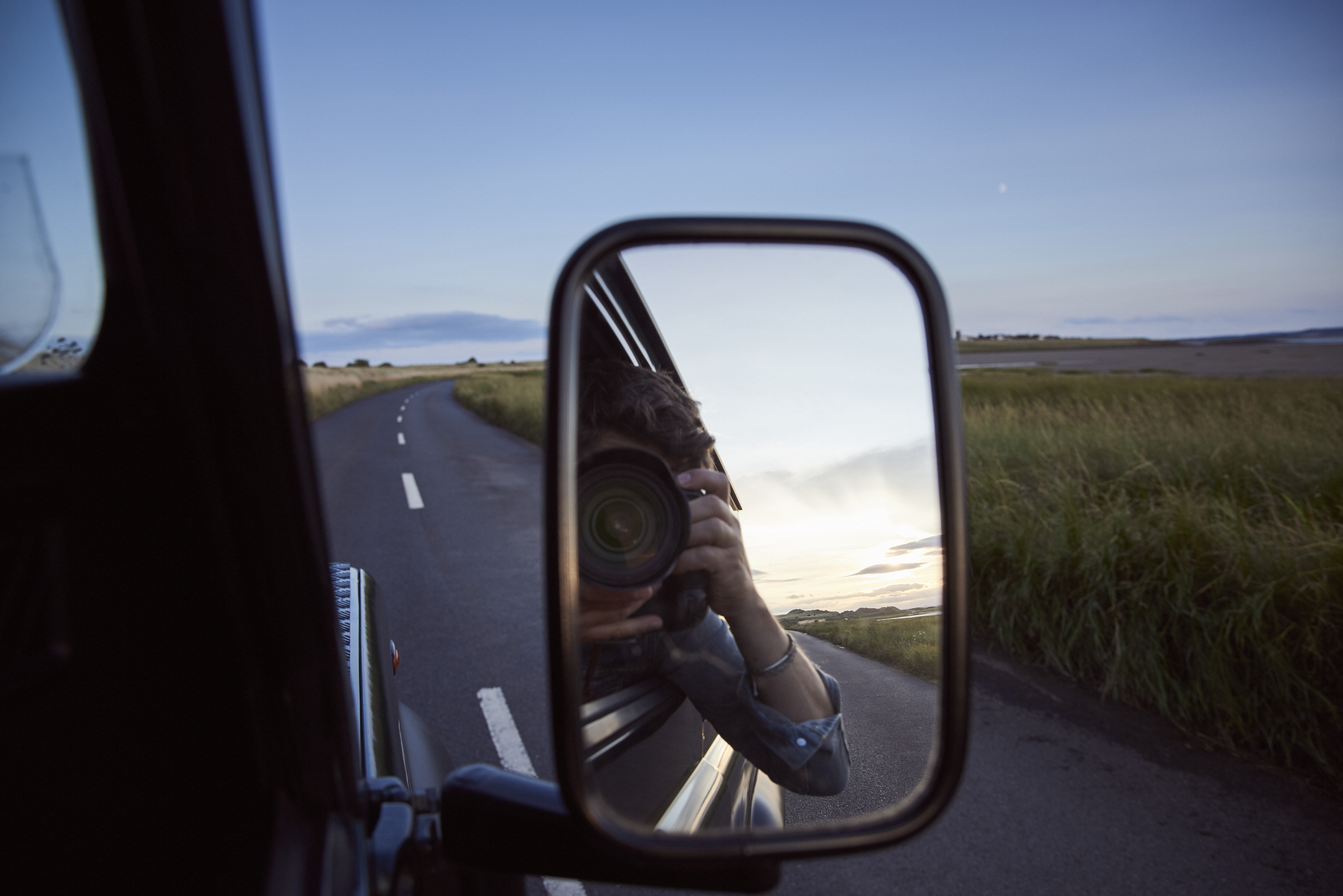 Reflection of a man with a camera in the side mirror of a car
