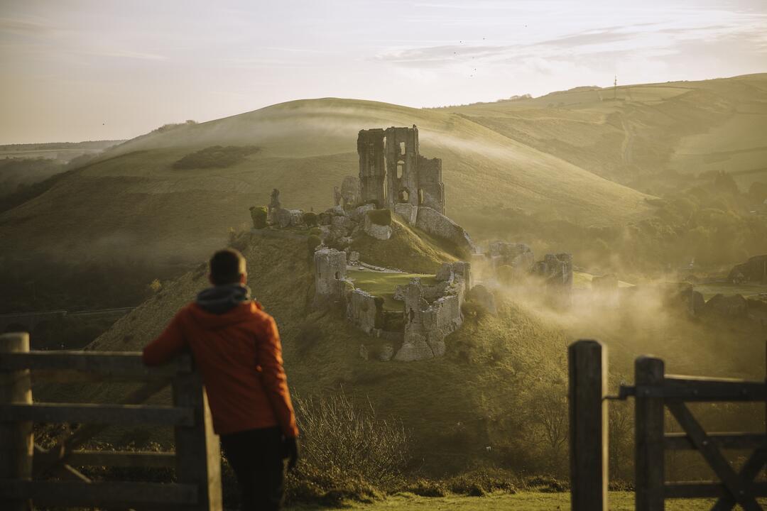 Man leaning on gatepost, looking at the ruins of a castle