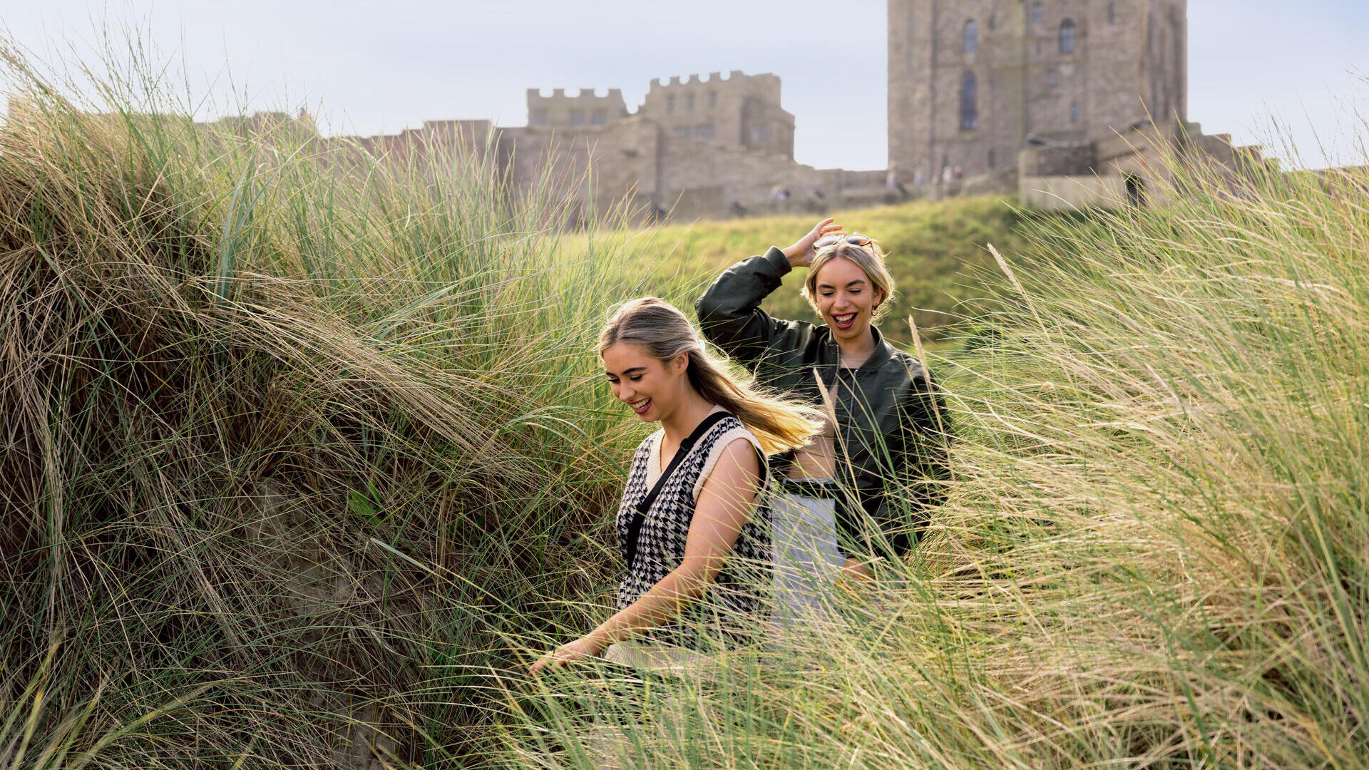 Zwei Frauen spazieren in den Sanddünen am Meer mit einer Burg im Hintergrund