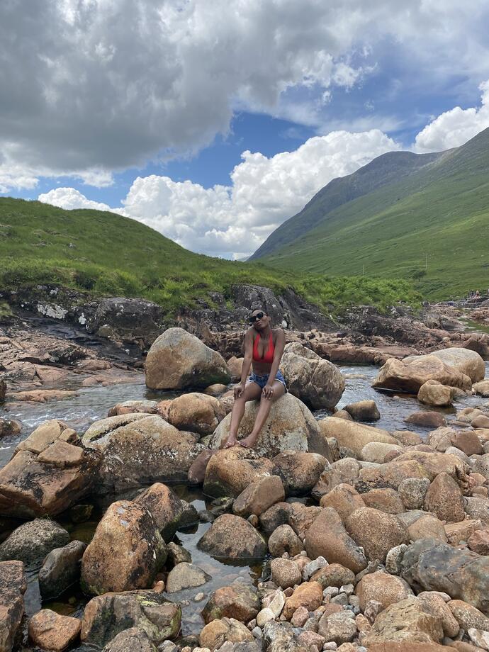 Femme assise sur un rocher dans un ruisseau entouré de montagnes
