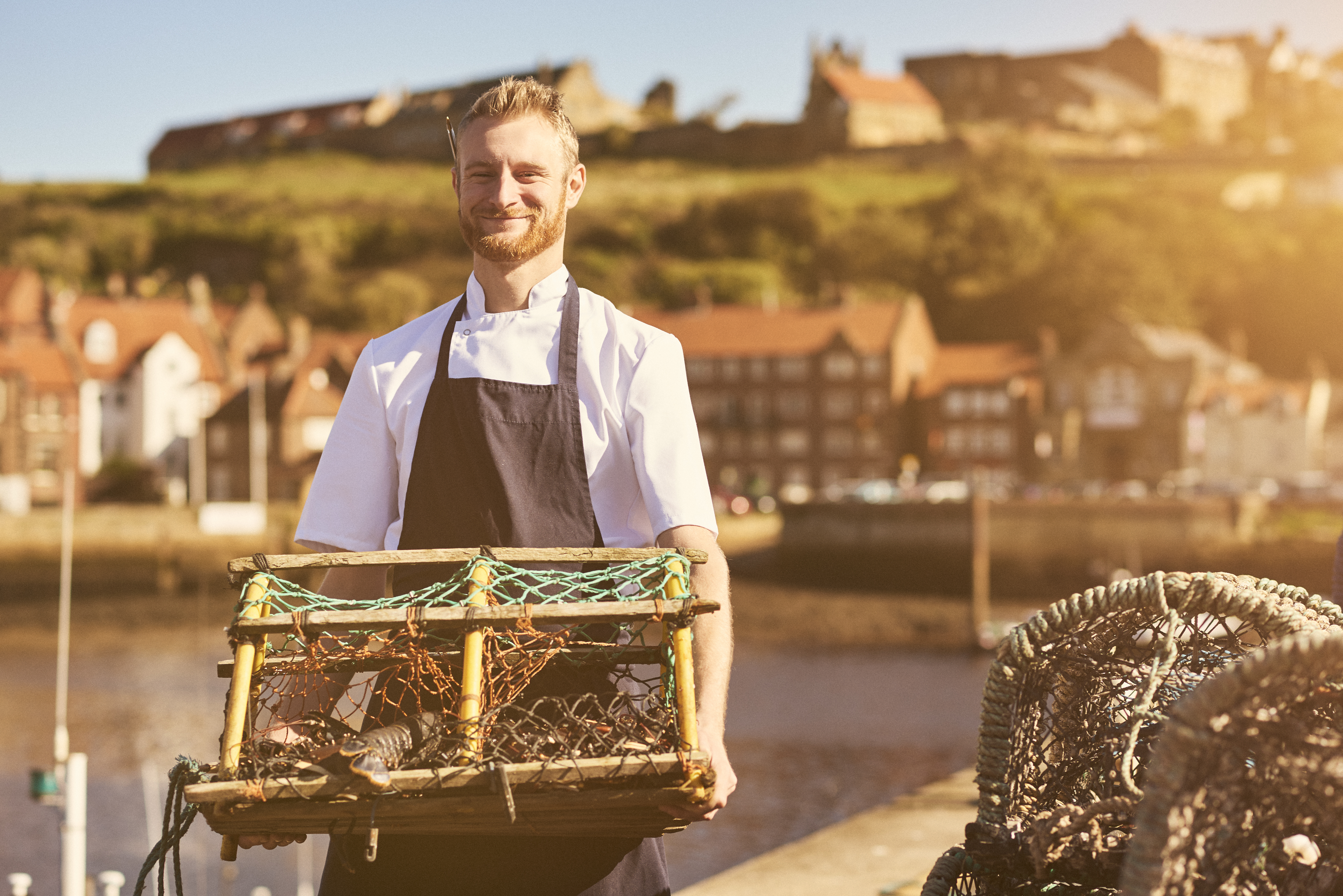 Man holding a lobster trap on a pier in the sunshine