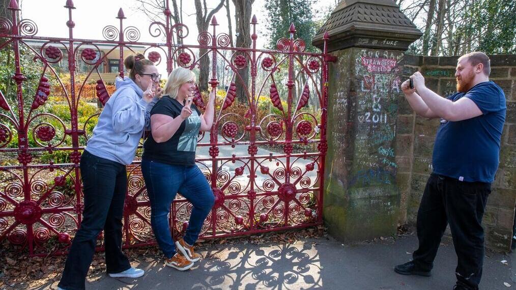 Two women pose in front of the red gates at the Strawberry Field garden.