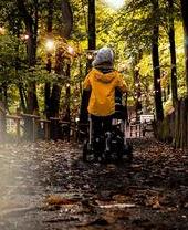 Une personne en imperméable poussant une poussette sur un sentier dans les bois