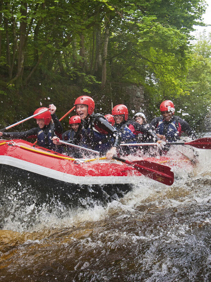 People wearing wetsuits and helmets paddling down a rapid