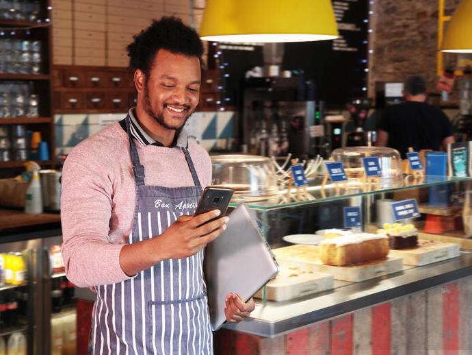 Male cafe owner smiling at his phone in front of the counter in the restaurant