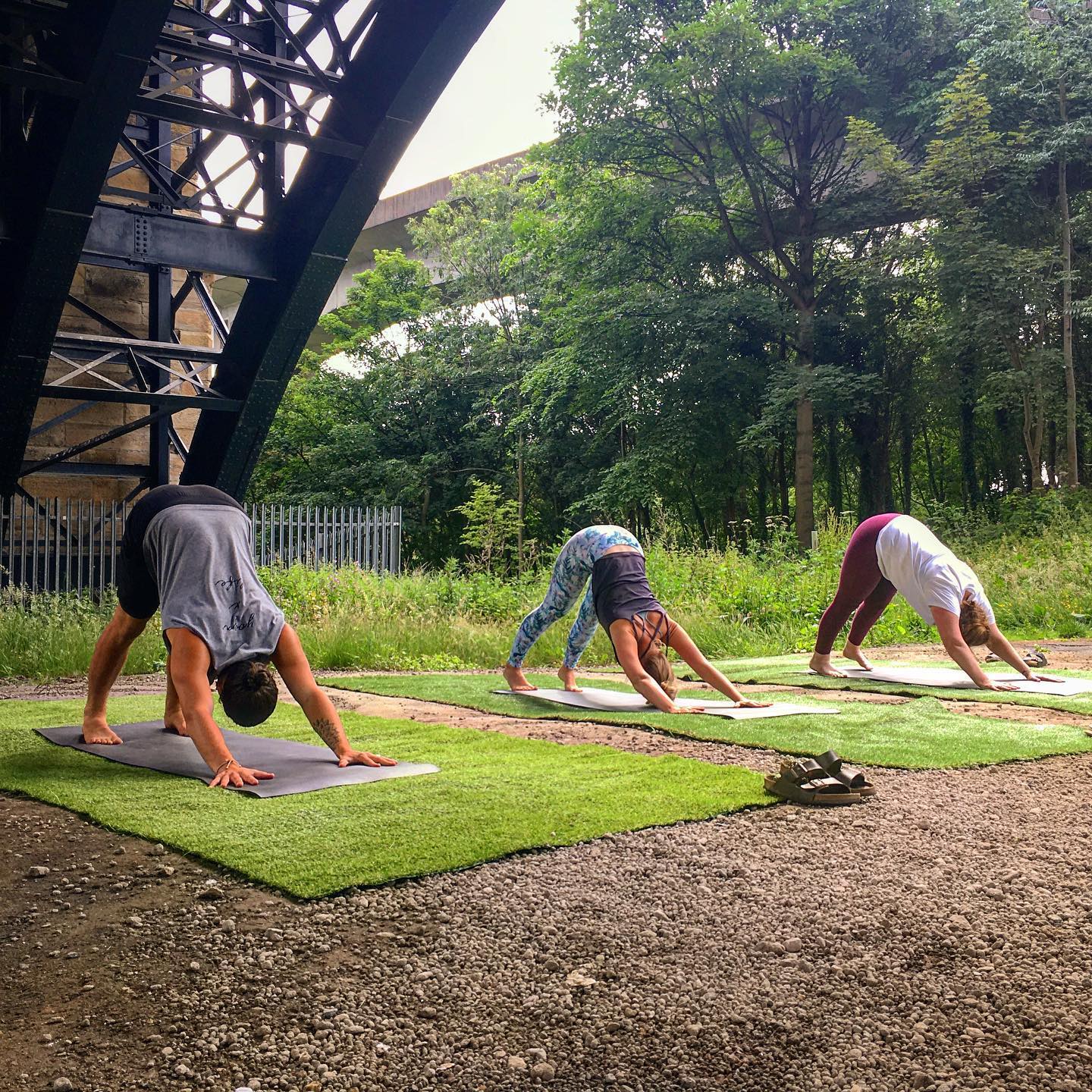 People practising yoga outside, beneath a bridge