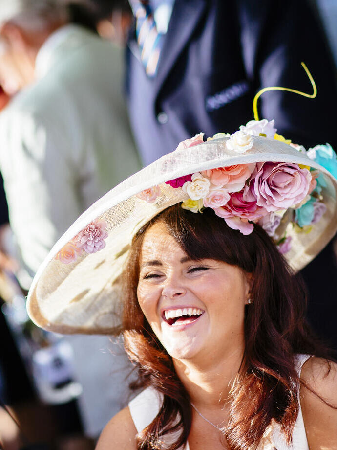 Royal Ascot Race Meeting at the prestigious Ascot racecourse in Berkshire. Smiling woman wearing a large hat with floral detail.